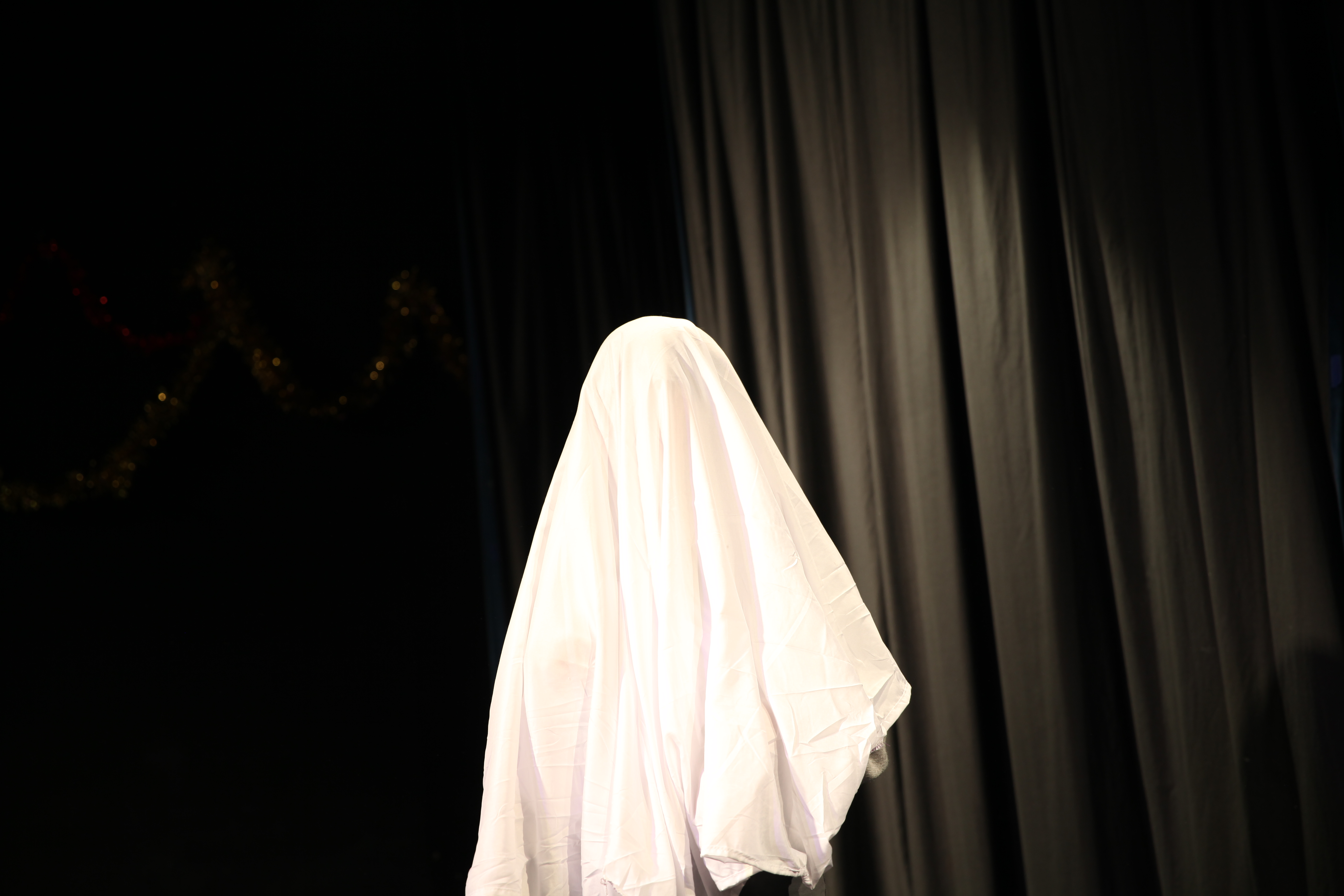 An actor wearing a white sheet, like a ghost, stands on stage.