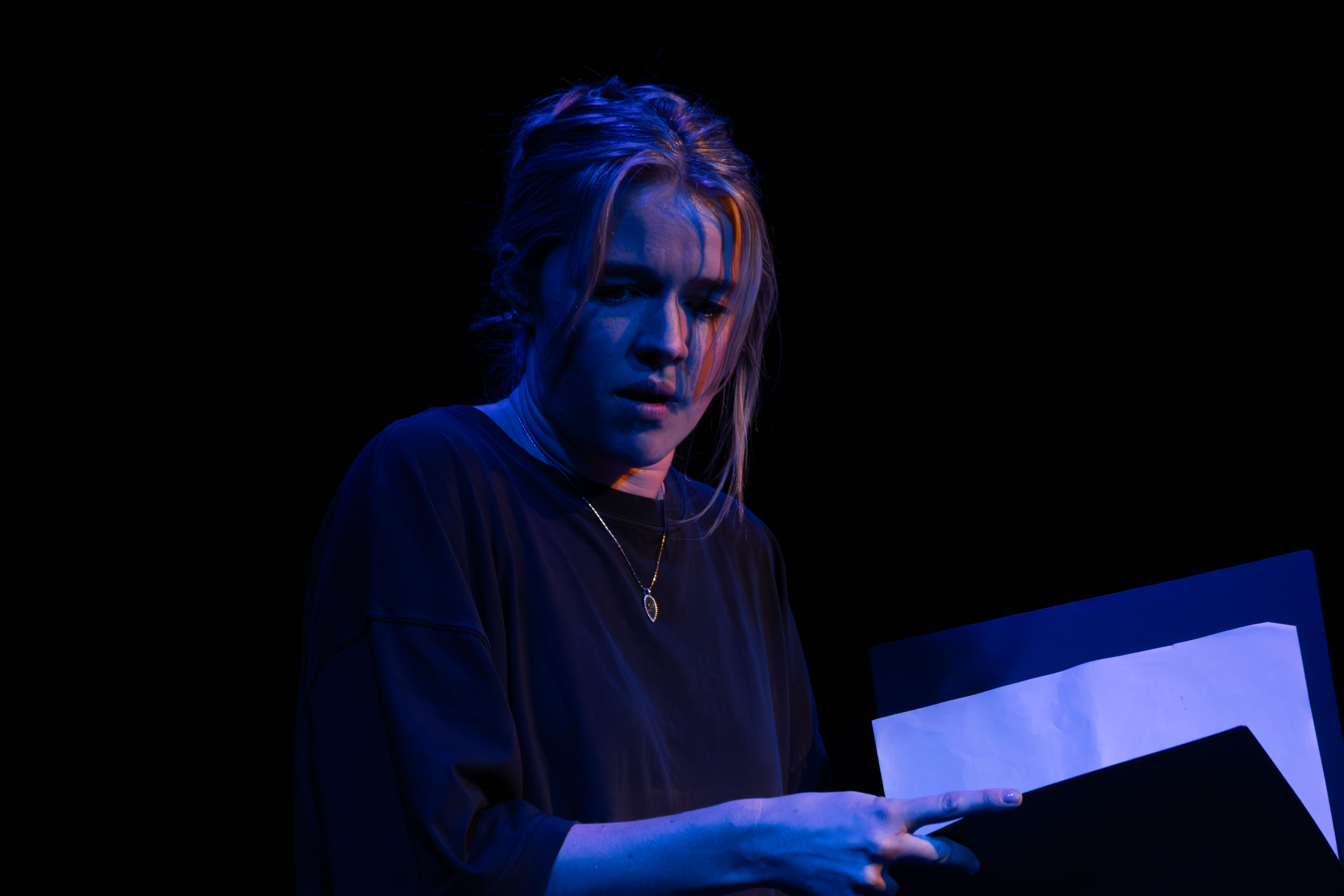 Liv onstage as Mag, looking down. Blue light.