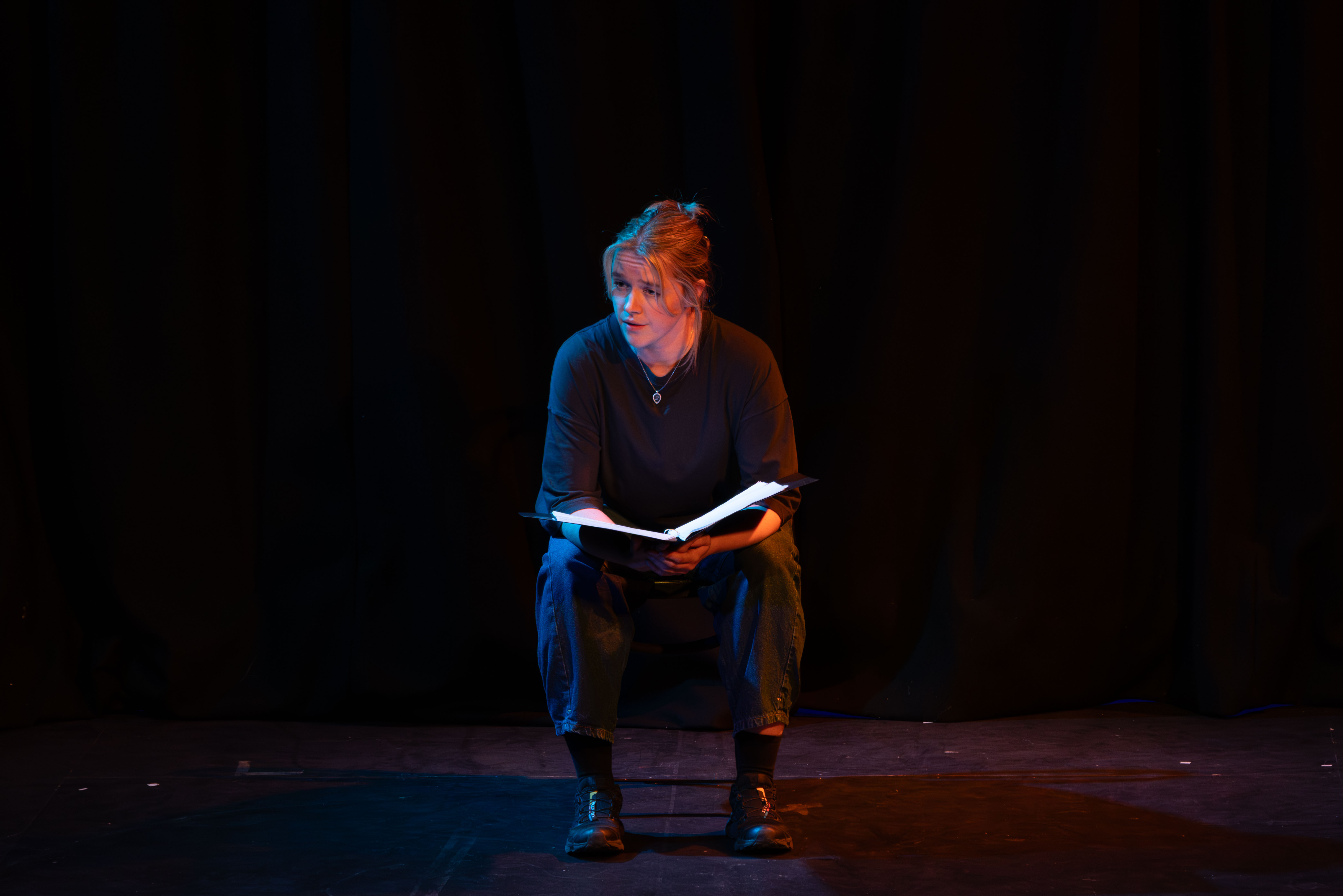 Liv onstage as Mag, seated. Teal and orange light.